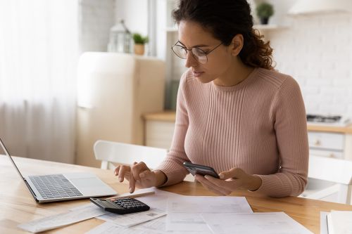 Foto: Frau mit Smartphone, Taschenrechner und Laptop